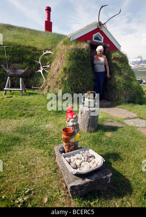 Una donna sta nel vano della porta del suo tappeto erboso tradizionale casa del villaggio di Borgarfjörður, Islanda Foto Stock