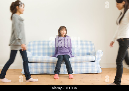 Una donna seduta su un divano e due donne a piedi Foto Stock