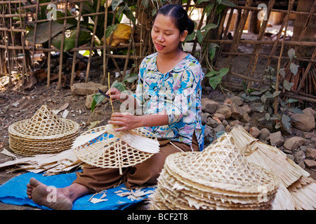 Myanmar Birmania Mrauk U. Una donna si applica abilmente guaine di bambù per la cornice di bambù di una conica, largo-colmato hat. Foto Stock