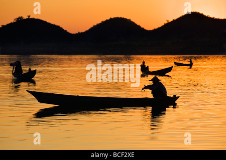 I pescatori immerso nella tonalità dorate del sole di setting come essi pesce da loro piccole imbarcazioni sul lay Myo fiume. Foto Stock