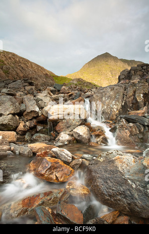 Snowdon nella luce del mattino con Afon Glaslyn in primo piano come si snoda su grossi massi vicino a Glaslyn al minatore Foto Stock
