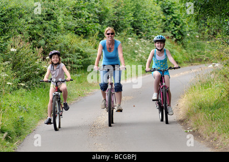 Ciclista femmina e i bambini a cavallo, lungo una strada di campagna Foto Stock