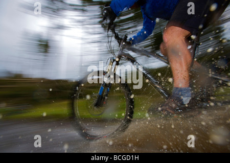 Ampio angolo di visione del ciclista pedalando attraverso una pozzanghera. Foto Stock