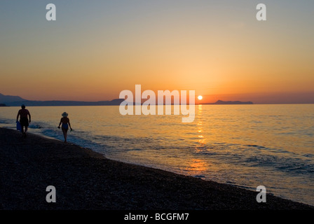 L uomo e la donna a piedi lungo una spiaggia tenendo le mani al tramonto Adelianos Kampos Foto Stock