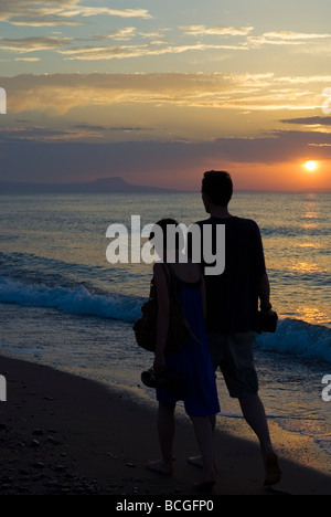 Uomo e Donna che camminano lungo una spiaggia tenendo le mani al Tramonto Adelianos Kampos Rethymnon Foto Stock