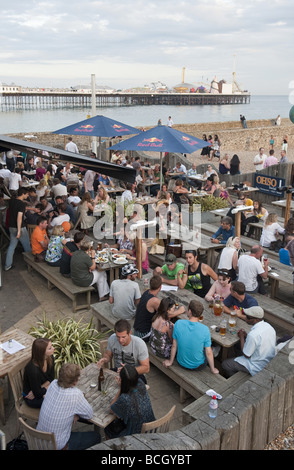 I giovani per i turisti e la gente del posto godersi una giornata di sole in un pub sulla spiaggia ristorante vicino al molo di divertimenti a Brighton cittadina balneare Foto Stock