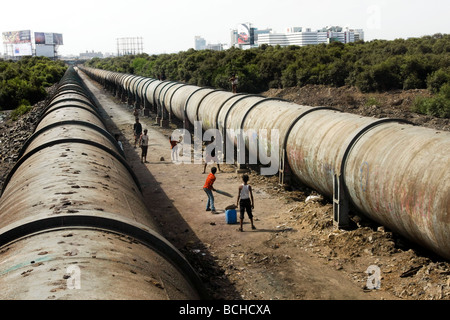 I bambini giocare a cricket tra due grandi waterpipes che corre attraverso Dharavi, la più grande delle baraccopoli di Mumbai (Bombay). Foto Stock