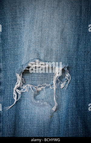 Dettaglio di un foro sfilacciata in ginocchio di un paio di jeans denim Foto Stock