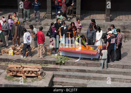 Pashupatinath, Nepal. Membro della famiglia luoghi ghirlanda di Le calendule dentro una bara di un defunto, legno per la cremazione Pira attende. Foto Stock