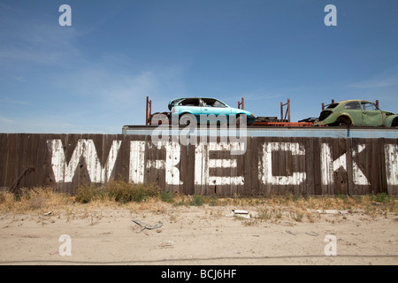 Parete di legno di auto demolizione salvage yard con word relitto dipinto su di esso Automobies veicoli dietro il recinto contro il cielo blu Foto Stock