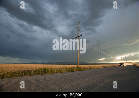 Carrello VEICOLO SUV automobile sulla sterrata strada di ghiaia rivestiti con poli di utilità al tramonto con drammatica sky Montana USA Foto Stock