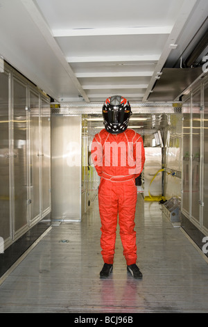 Race Driver auto indossando il casco e rosso vestito di salto in piedi all'interno di metallo del veicolo di trasporto Foto Stock