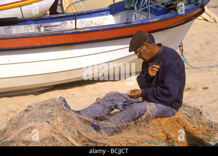 Fisherman riassettando le reti sulla spiaggia di Armacao de Pera in Algarve Foto Stock