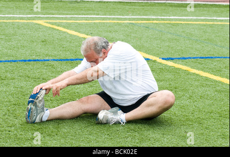 Il sovrappeso medioevo ritirato e attivo uomo senior il suo stiramento dei muscoli della gamba dopo aver esercitato su un campo sportivo all'aperto Foto Stock