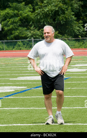 Il sovrappeso medioevo ritirato e attivo uomo senior il suo stiramento dei muscoli della gamba dopo aver esercitato su un campo sportivo all'aperto Foto Stock