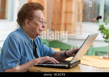 Vecchia donna con un computer portatile scrive e-mail Foto Stock