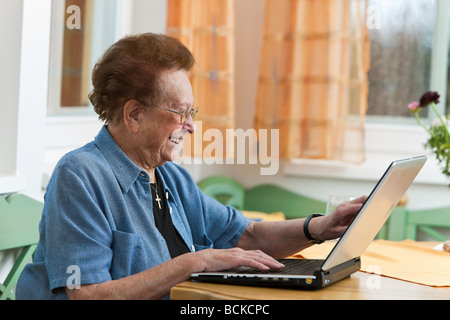 Vecchia donna con un computer portatile scrive e-mail Foto Stock