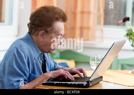 Vecchia donna con un computer portatile scrive e-mail Foto Stock