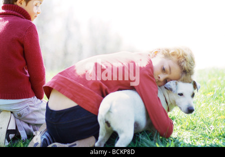 Bambini seduti su erba, abbracciando un cane Foto Stock