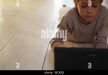 Bambino giacente sul piano guardando il computer portatile Foto Stock