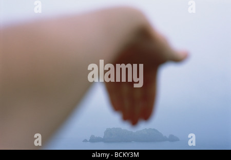 Persona la mano, offuscata, nella parte anteriore delle rocce in mare Foto Stock