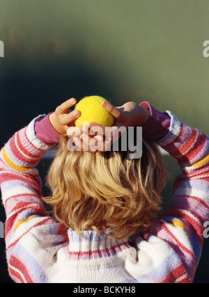 Bambino tenendo palla da tennis sopra la testa, vista posteriore Foto Stock