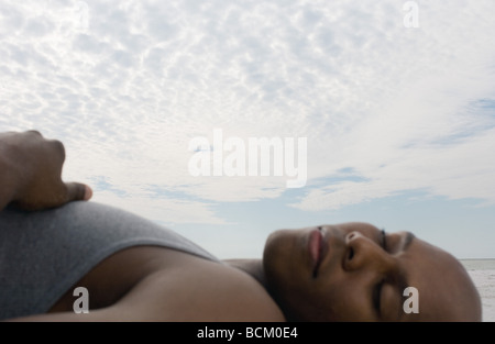 Uomo dorme vicino oceano, concentrarsi su sky in background Foto Stock