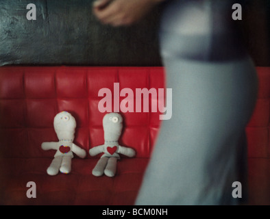 Donna che cammina da due bambole di pezza sul divano rosso, focus su bambole in background Foto Stock