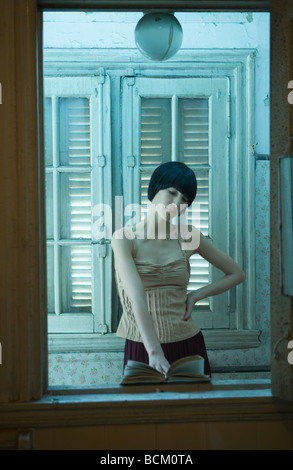 Donna in piedi, libro di lettura con la mano sulla hip, riflesso dello specchio Foto Stock