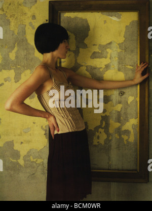Donna in piedi accanto a vuoto cornice immagine appesa sul muro, mano su hip Foto Stock