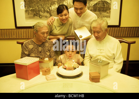 Tre generazioni la famiglia avente festa di compleanno per la ragazza, ragazza soffiando le candeline sulla torta Foto Stock