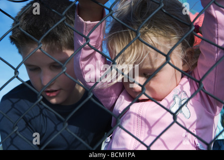 Un ragazzo e una ragazza guardando attraverso la recinzione ad anelli, close-up Foto Stock