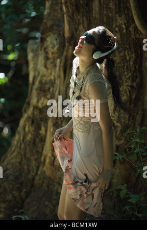 Giovane donna ascoltando le cuffie all'aperto, danze, bocca aperta Foto Stock