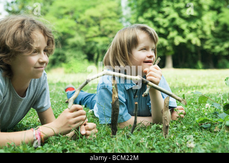 Due ragazze giacente su erba, tenendo bastoni, sorridente, uno con la sindrome di Down Foto Stock