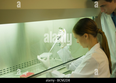 Donne scienziato che lavora in laboratorio, il collega di sesso maschile guardando sopra la sua spalla, vista laterale Foto Stock