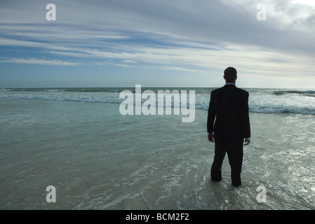 Imprenditore in piedi in mare, fissando orizzonte Foto Stock