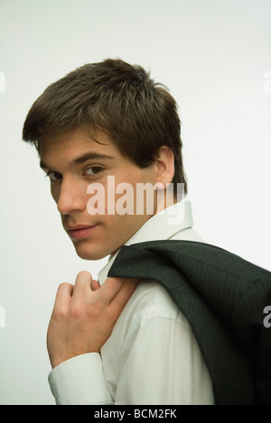 Giovane uomo camicia di contenimento, guardando sopra la spalla in telecamera Foto Stock