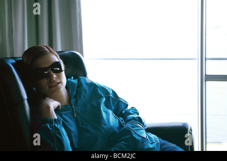 Donna slouching in poltrona, indossando occhiali da sole Foto Stock