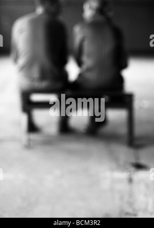 L uomo e la donna seduta sul banco, parlando, vista posteriore, sfocato Foto Stock