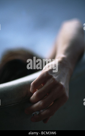 Uomo seduto in poltrona, tenendo sigaretta dietro la testa Foto Stock