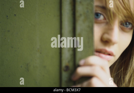 Giovane donna spiata attorno allo sportello, close-up, ritratto Foto Stock