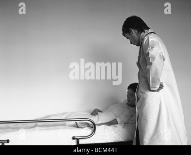 Donna sdraiata nel letto di ospedale, dottore in piedi dal suo lato Foto Stock