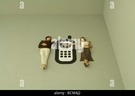 Coppia giacendo a terra con un grande telefono cellulare tra di loro, tenendo le mani Foto Stock