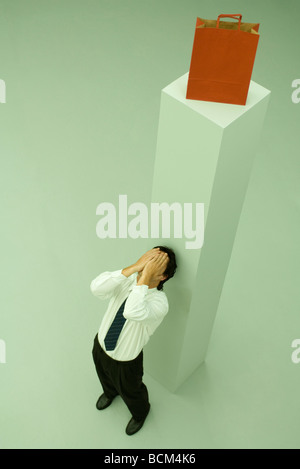 Uomo appoggiato a alto piedistallo con shopping bag sulla parte superiore, le mani sul viso Foto Stock