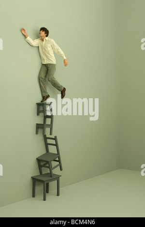 Uomo in piedi sulla sommità di una pila di sedie e tavoli e un braccio sollevato Foto Stock