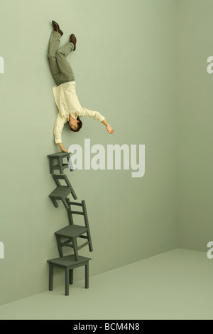 Uomo in equilibrio su una mano su alta pila di sedie Foto Stock