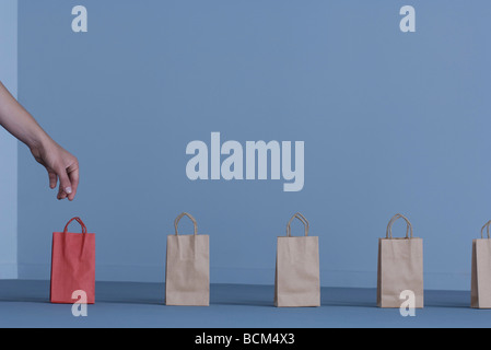 Carta Sacchetti regalo in una fila, donna la mano per raggiungere solitario sacchetto rosso Foto Stock