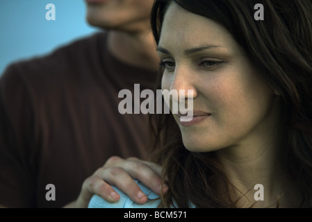 Donna che guarda lontano, sorridente, mano d'uomo sulla sua spalla Foto Stock