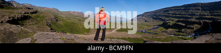 Panoramica di una donna escursionista guardando giù per la valle di Berufjordur in Islanda verso il fiordo di Berufjordur Foto Stock