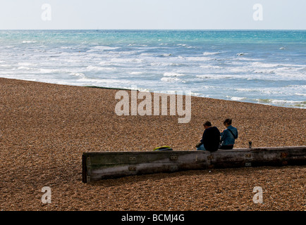 Due persone sedute su una struttura di frangionde sulla spiaggia di ciottoli in Brighton nel Sussex. Foto di Gordon Scammell Foto Stock